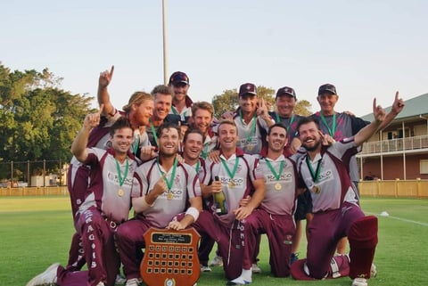 Maroon and white uniformed softball team celebrating championship win with trophy on field